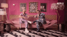 two men are sitting on a pink couch with netflix written on the bottom of the screen