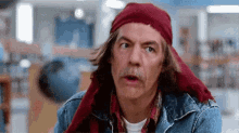 a man with long hair and a mustache is wearing a red head scarf .