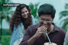 a man is drinking a coconut milkshake with a straw while a woman looks on .