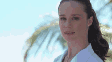a woman wearing a white shirt and earrings is standing in front of a palm tree .