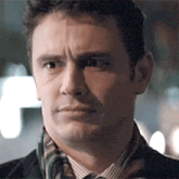 a man wearing a scarf and a suit is looking at the camera