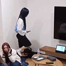 a woman is standing on a chair in a living room while another woman sits on a couch .