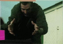a man in a green jacket reaches out his hands
