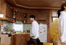 a man in a white shirt is standing in a kitchen with a brick wall and a refrigerator