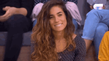 a woman with curly hair is smiling while sitting in a crowd