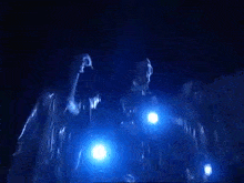 a group of people are dancing in a dark room with a blue light behind them