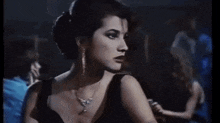 a woman in a black dress and necklace is standing in a dark room in a club .
