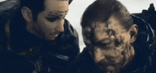 two men are standing next to each other with their faces painted . one of the men has a tattoo on his forehead .