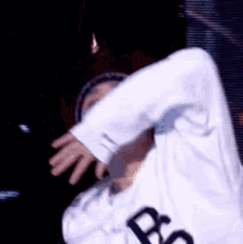 a person wearing a white shirt with the letter b on it is dancing on a stage in a dark room .