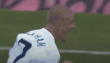 a soccer player wearing a white jersey with the number 7 on it is celebrating a goal on a soccer field .