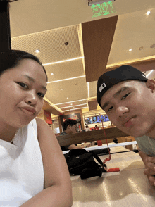 a man and a woman sitting at a table in front of an exit sign