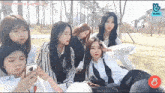a group of girls are sitting in a park and looking at their phones .