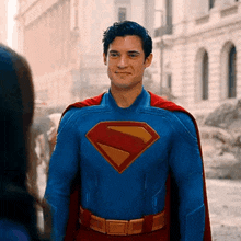 a man in a superman costume is smiling while standing on a street .
