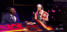 alexa bliss is holding a wrestling championship while talking to a man in a suit on a wrestling show .