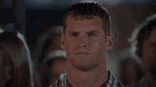 a man in a plaid shirt is making a funny face in front of a crowd .