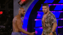 two wrestlers are standing next to each other on a stage and shaking hands .