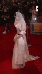 a woman in a white dress is walking on a red carpet