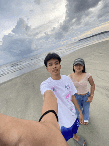 a man and a woman are standing on a beach and the man is wearing a white shirt that says " tasty girl "