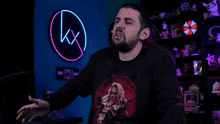 a man with a beard wears a black shirt with a wanted sign in the background