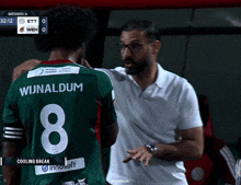 a man in a white shirt is talking to a soccer player in a green jersey with the number 8 on it