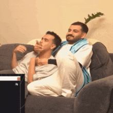 two men are sitting on a couch and one of them is covering his mouth