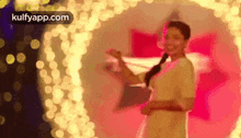 a woman in a white dress is standing in front of a heart shaped wall of lights .