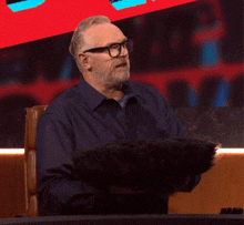 a man with glasses and a beard is sitting at a desk holding a black object