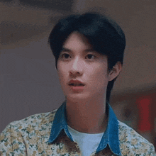 a young man wearing a floral shirt and a denim collar is looking at the camera .