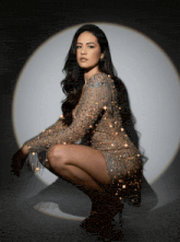 a woman in a sparkly dress is squatting down in front of a spotlight