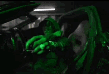 a man wearing a green watch is sitting in a car with a green light behind him .
