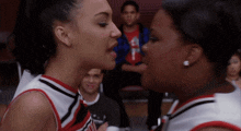 two cheerleaders face to face with one wearing a jersey that says ' nc state ' on it