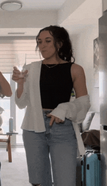 a woman in a black tank top and blue jeans holds a glass of wine
