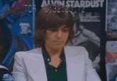 a man in a white suit stands in front of a poster that says alvin stardust