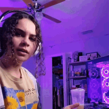 a woman wearing headphones is standing in front of a computer with purple lights