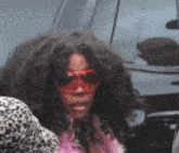 a woman with long curly hair is wearing red sunglasses and a pink jacket .
