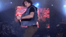 a man in a denim vest is singing into a microphone on a stage