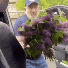 a man is holding a bouquet of purple flowers in his hand