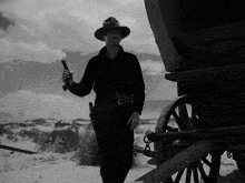 a black and white photo of a man holding a gun in front of a wagon