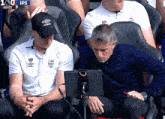 a man in a umbro hat sits next to another man in a white shirt