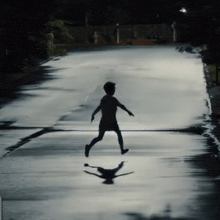 a silhouette of a child walking down a wet street at night