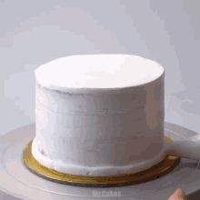 a cake is being frosted with white frosting and the word mr.cakes is visible on the bottom