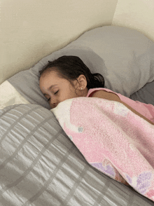a little girl is sleeping on a bed with a pink and white blanket