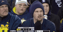 a man wearing a hat with the letter m on it watches a football game