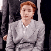 a man with red hair is wearing a suit and tie and sitting down .