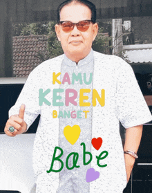 a man wearing sunglasses and a shirt that says kamu keren banget babe is giving a thumbs up