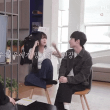 a woman sits on a chair next to a man with korean writing on the wall