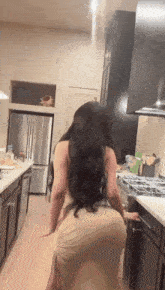 a woman in a long dress is standing in a kitchen with a stove .