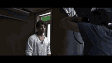 a man in a white shirt is being photographed by a cameraman in a dark room .