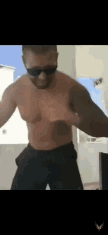 a shirtless man wearing sunglasses is standing in front of a window .