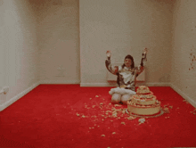 a woman is sitting on a red carpet with a cake on the floor